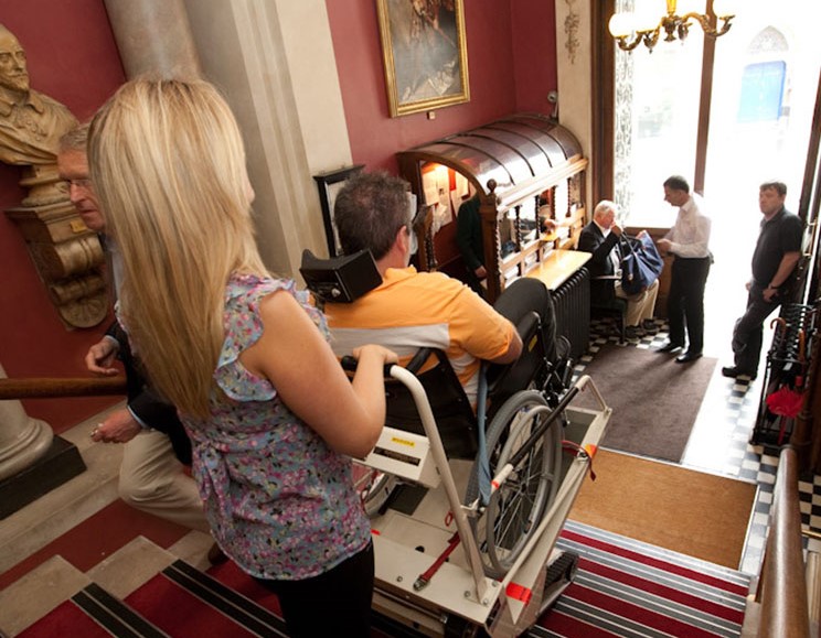 Operator using a Stairmate Major stairclimber to transport a passenger down a flight of stairs at the Garrick Club, London